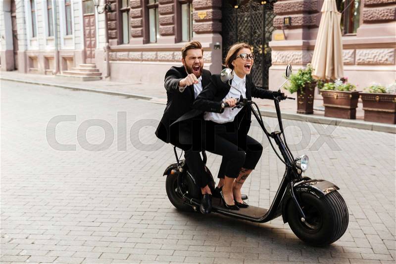 Excited young couple wearing smart clothes riding motor bicycle on a city street, stock photo