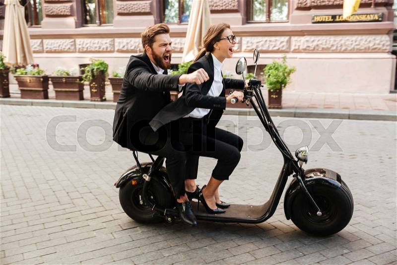 Happy excited couple wearing smart clothes riding motor bicycle on a city street, stock photo