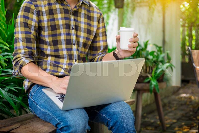 Man on week-end working on laptop computer outdoor in a park garden during a sunny summer day, stock photo