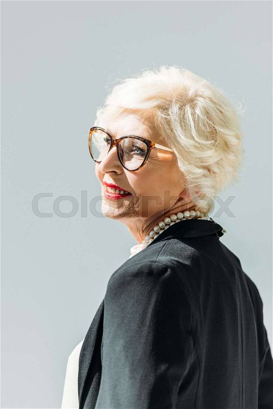 Attractive elegant smiling senior lady with pearl necklace, isolated on grey, stock photo