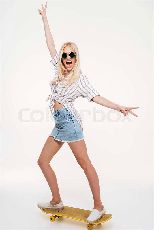 Full length portrait of a crazy cheerful blonde woman riding a skateboard isolated over white background, stock photo
