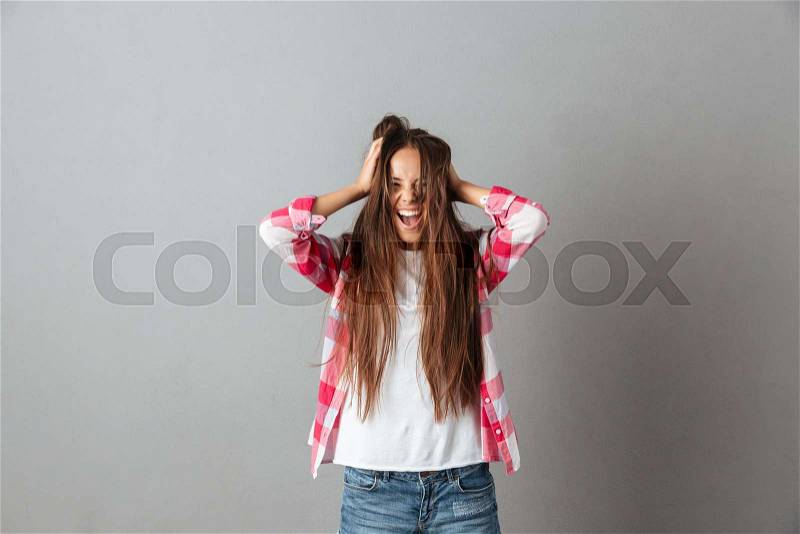 Photo of young long haired woman screaming and touching hair, over grey background, stock photo