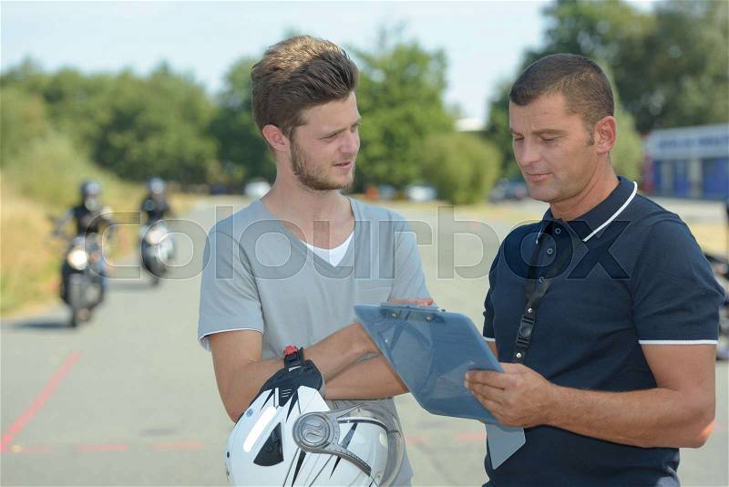 Young man talking to instructor of motorcycle training course, stock photo
