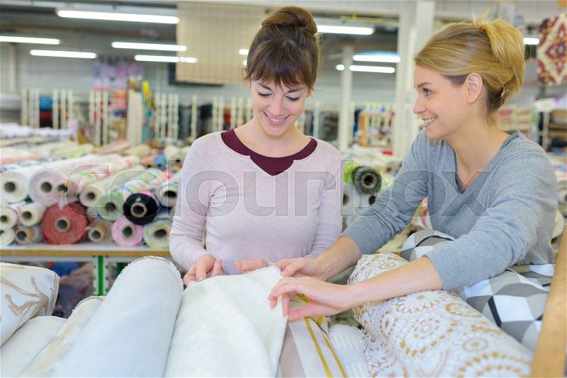 Smiling brunette choosing fabric skeins in textile shop, stock photo