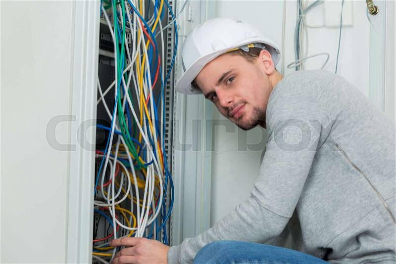 Portrait of young electrician wiring an electric panel, stock photo