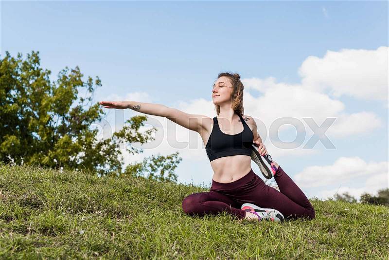 Young woman in One-legged king pigeon pose practicing yoga outdoors, stock photo