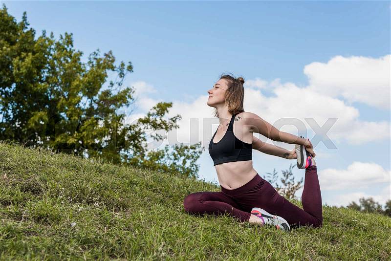 Fit woman in One-legged king pigeon pose practicing yoga outdoors , stock photo