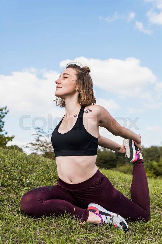 Happy fit woman in One-legged king pigeon pose practicing yoga outdoors , stock photo