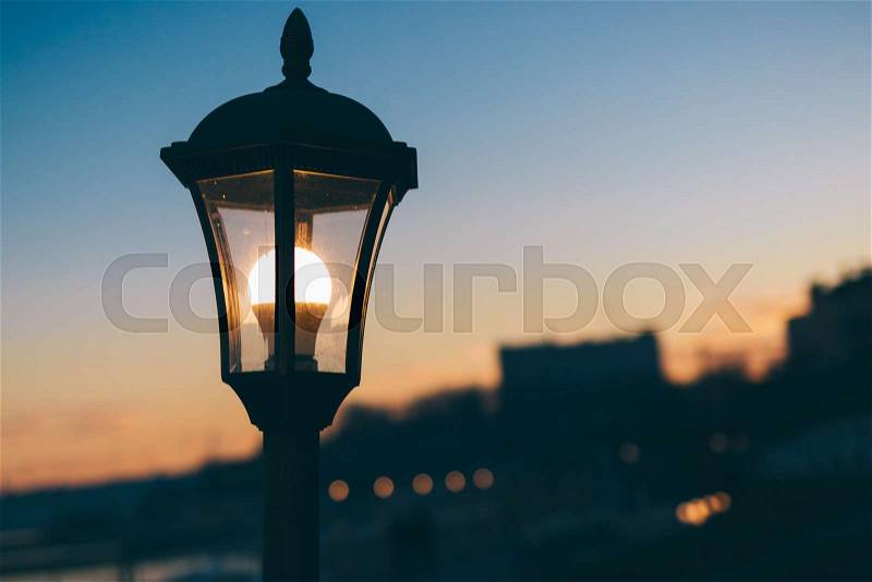Glowing street lamp against the backdrop of the city and sky, stock photo