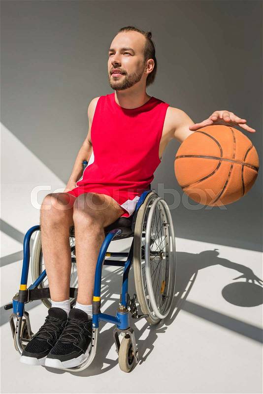 Happy young sportsman in wheelchair dribbling basketball ball, stock photo