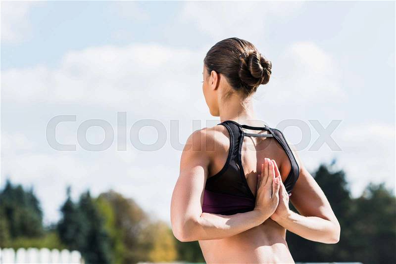 Fit yogini in Reverse Prayer Pose practicing yoga outdoors, stock photo