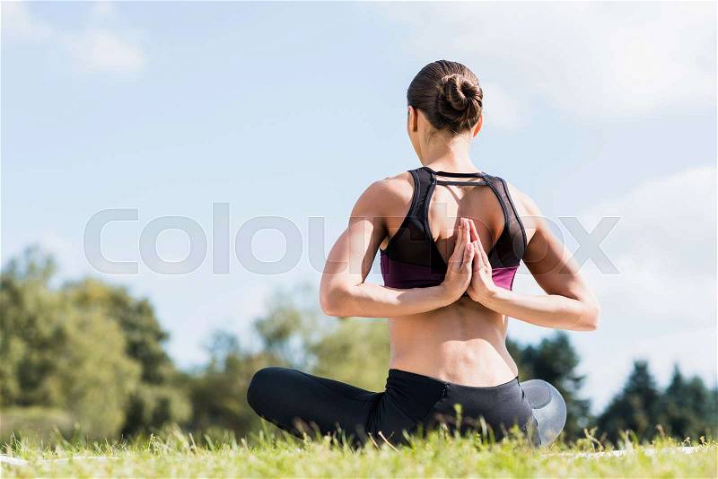 Young yogini in Reverse Prayer Pose practicing yoga outdoors, stock photo