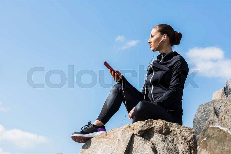 Beautiful fit woman sitting on rocks and listening music, stock photo
