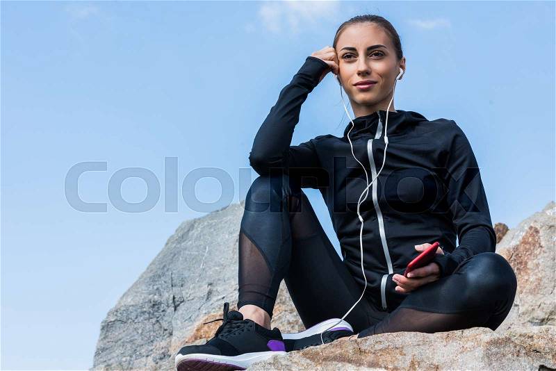 Beautiful fit woman sitting on rocks and listening music, stock photo