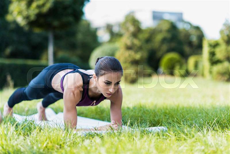 Young sportive woman doing plank exercise on grass in park, stock photo