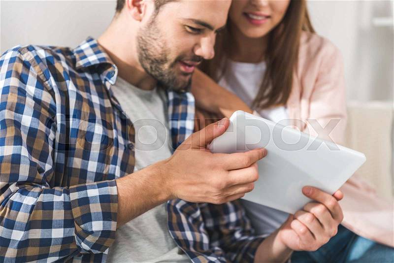 Young attractive couple using digital tablet and sitting on sofa together at home, stock photo