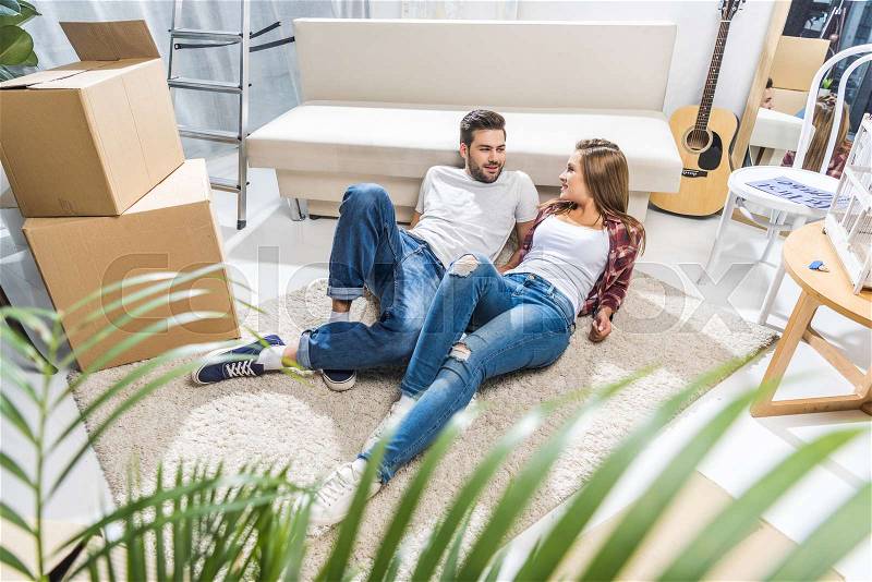 Young attractive couple relaxing together on floor in living room, stock photo