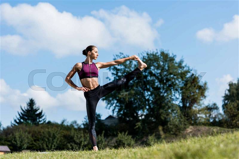 Fit woman in big toe pose practicing yoga outdoors, stock photo