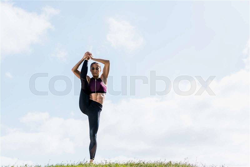 Young woman standing on one leg with other raised practicing yoga outdoors, stock photo