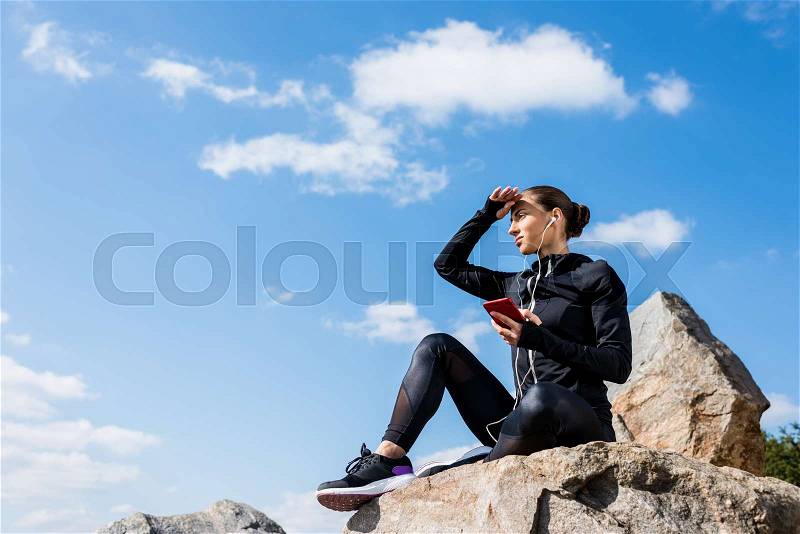 Young relaxed woman sitting on rocks and listening music, stock photo
