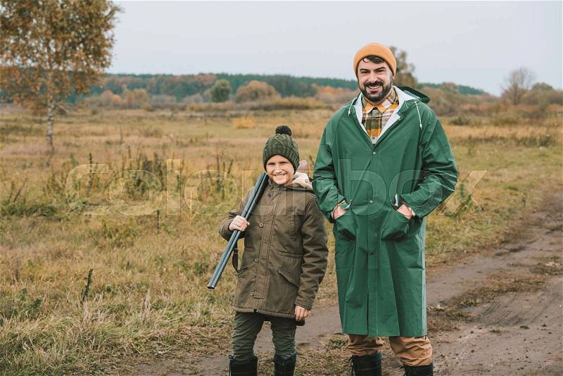 Father and son with a gun posing to camera on a nature, stock photo