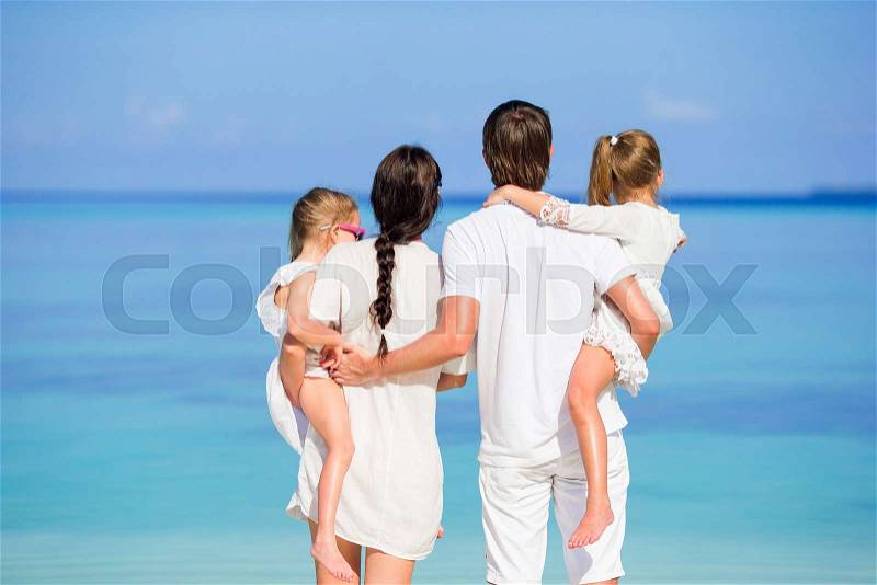 Back view of a happy family in white on the beach, stock photo