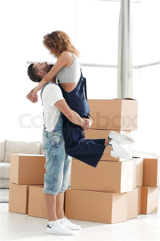 Husband hugs a happy wife against the background of large cardboard boxes, stock photo