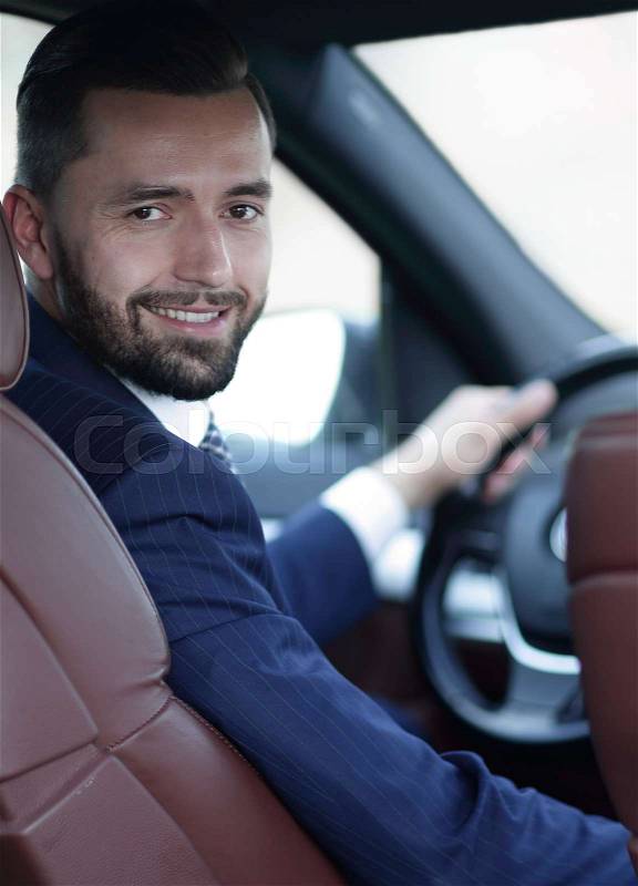 Successful businessman sitting at the wheel of a car and looking at the camera, stock photo
