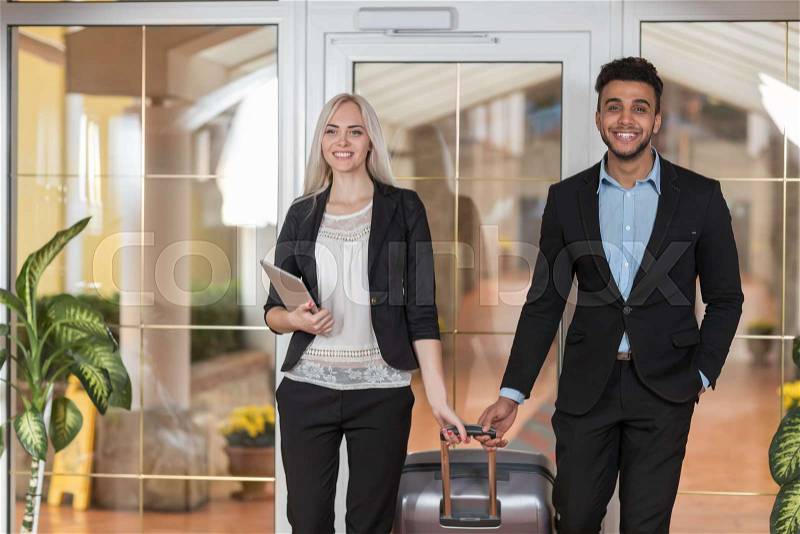 Smiling Business Couple In Hotel Lobby, Businesspeople Group Man And Woman Guests Arrive Entrance With Suitcase, stock photo