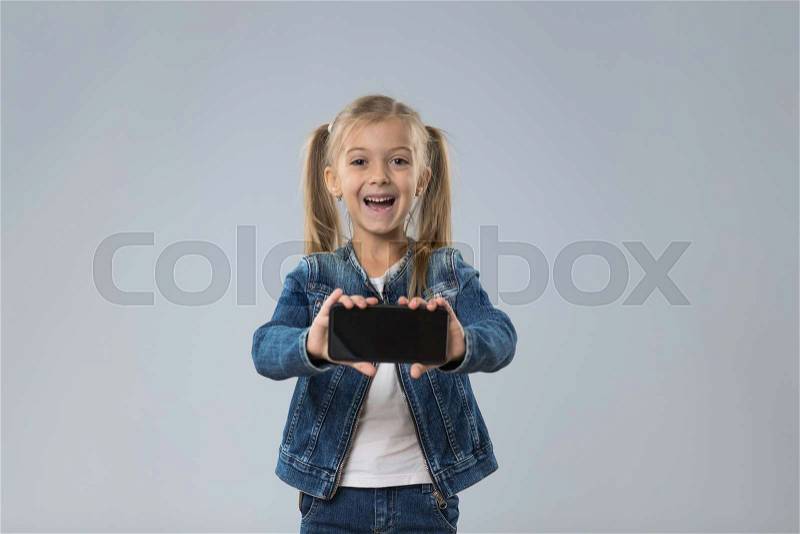 Little Teenage Girl Show Cell Smart Phone Screen With Empty Copy Space, Small Excited Happy Smiling Child Isolated Over Gray Background, stock photo