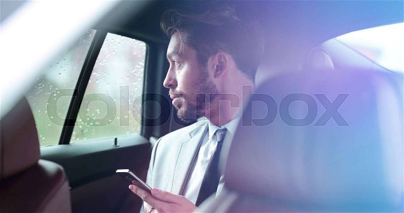 Handsone successful businessman using mobile phone in back seat of car, stock photo