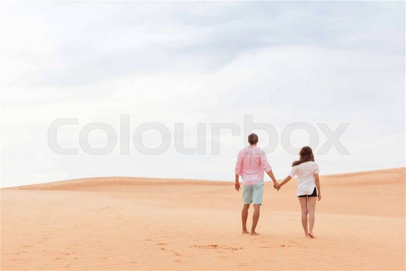 Young Man Woman Walking In Desert Couple Girl And Man Hold Hands Back Rear View Sand Dune Landscape Nature Background, stock photo
