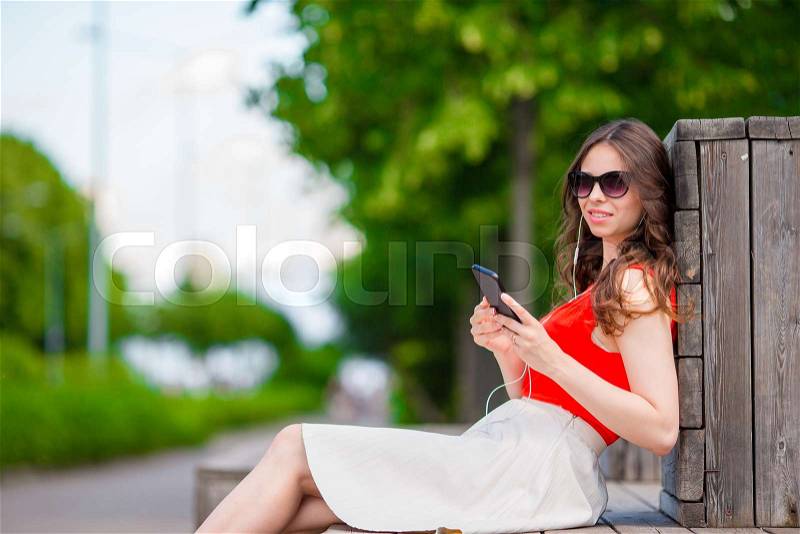 Beautiful girl listening music by smartphone on summer holidays. Young attractive tourist with mobile phone outdoors enjoying holidays, stock photo