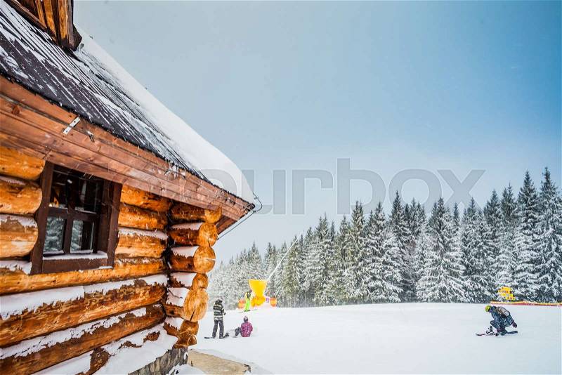 Winter vacation holiday wooden house in the mountains covered with snow. Pine trees forest and blue sky in the background. Active people with ski, snowboad. Sport, recreation. Bukovel resort, Ukraine, stock photo