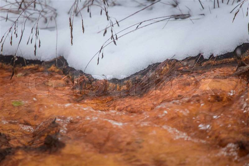 An orange rusty water at the old copper mine in Norway in winter. Bright color stream details, closeup, stock photo