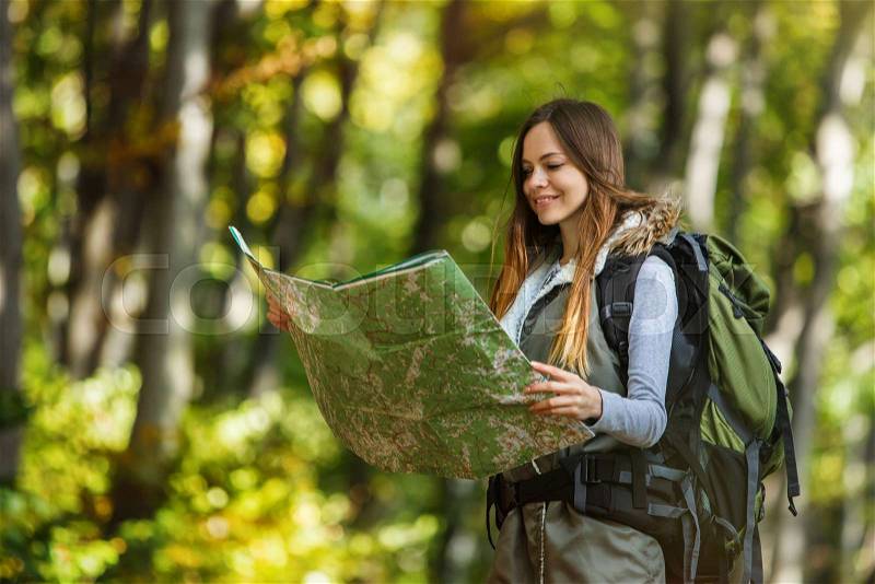 Cheerful brunette tourist backpacked girl have walk through forest holding map, autumn tourism concept, stock photo