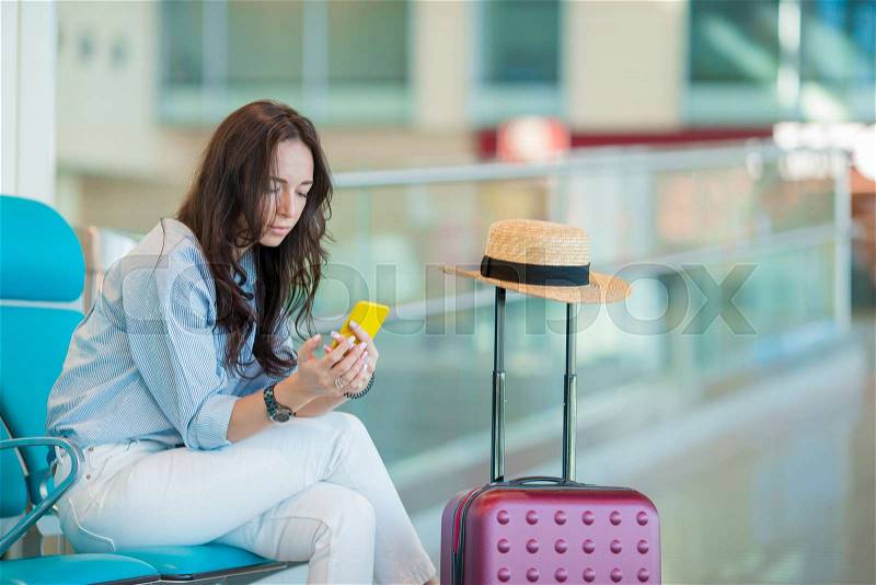 Young woman with smartphone in international airport waiting for flight aircraft, stock photo