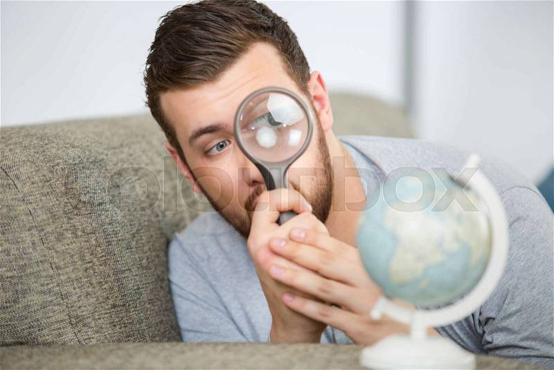 Man considering a world globe with a magnifying glass, stock photo