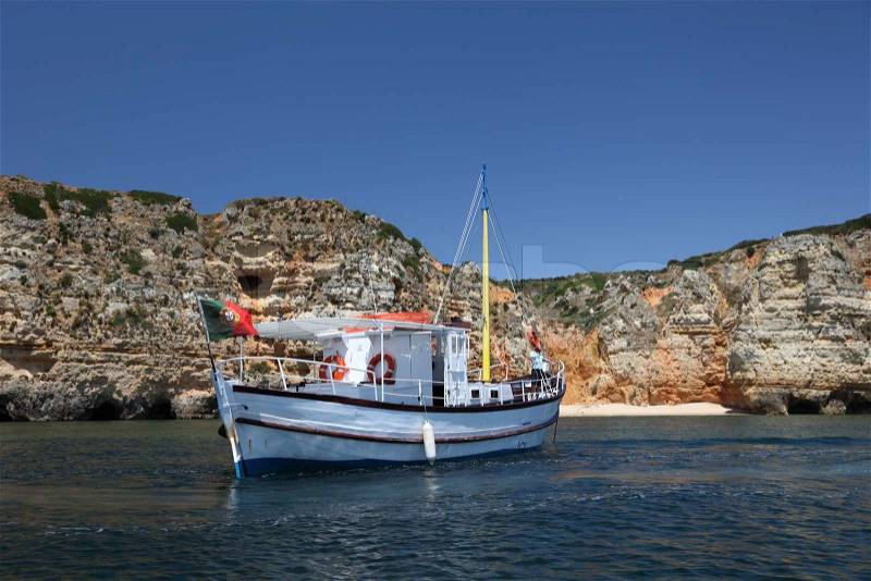 Fishing boat in front of the cliffs, Algarve Portugal, stock photo