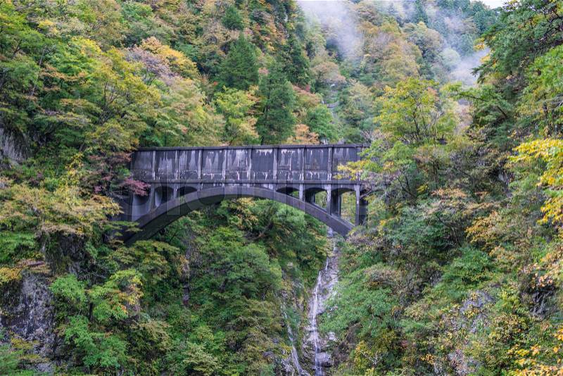 Aged black bridge for train on cliff with colorful orange and yellow leaves and tree in Unazuki onsen, Kurobe Japan in starting Autumn, stock photo
