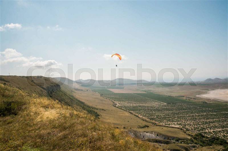 Person flying on paraglider, sky and field on background, stock photo