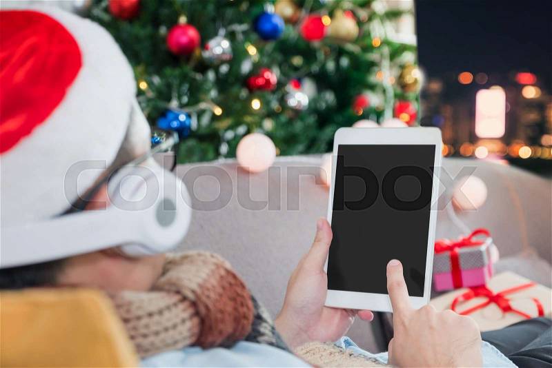 Man celebrate new year watching video on tablet ,Happy people lay on sofa and countdown from home with Christmas tree at night,Holiday celebration with technology,Blank screen for adding your design, stock photo