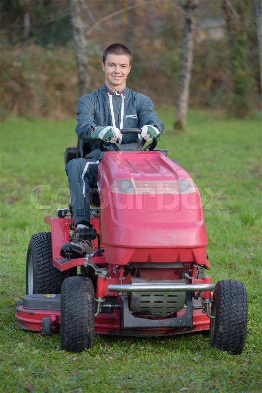 Young gardener on a lawn tractor, stock photo