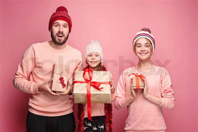 Father and mother give gifts to little daughter at pink studio background, stock photo