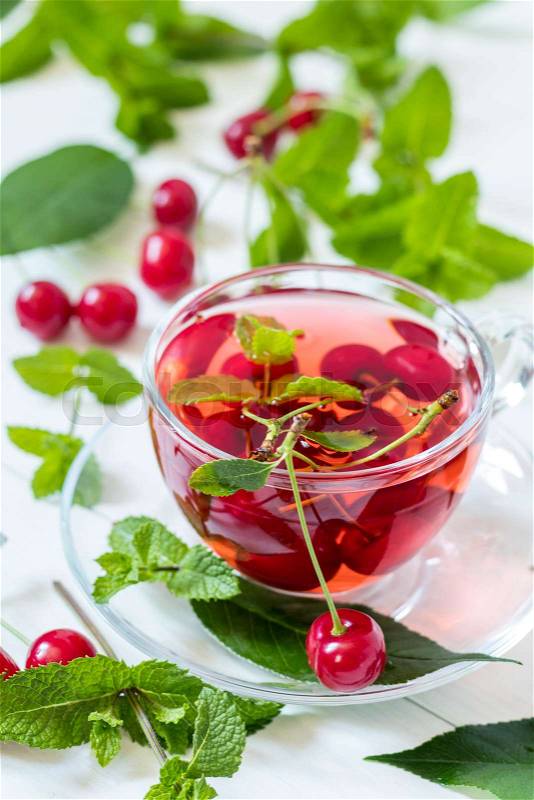 Fresh fruit cherry drink in transparent glass cup surrounded by cherries on the white wooden background, stock photo