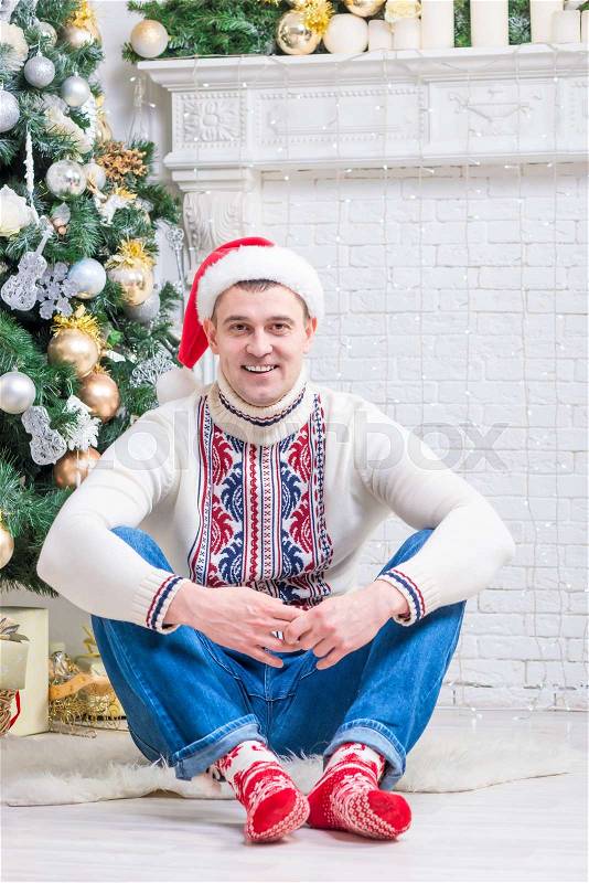 Nice man in a sweater and New Year\'s socks sitting near a Christmas tree, stock photo