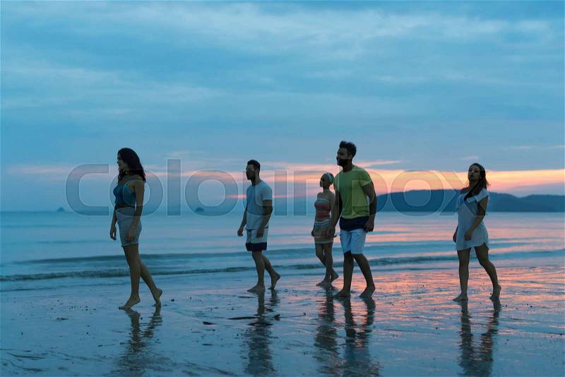 People Talking On Beach At Sunset, Young Tourist Group Walking On Sea In Evening Communication While Summer Vacation, stock photo