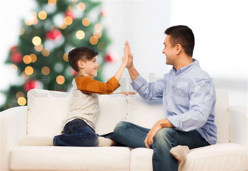 Family, gesture and people concept - happy father and son doing high five at home over christmas tree background, stock photo