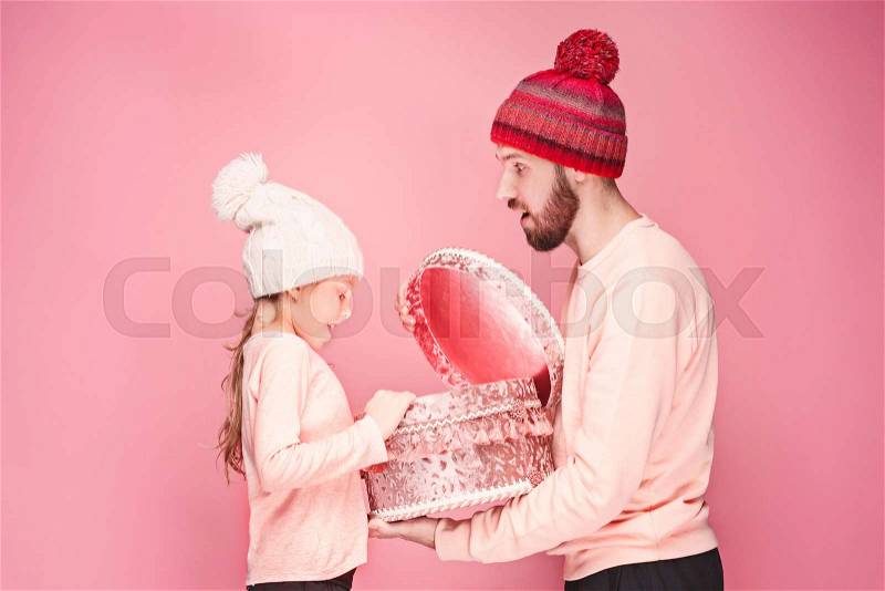 Portrait of a surprised little girl with her father holding a Christmas present at pink studio background, stock photo