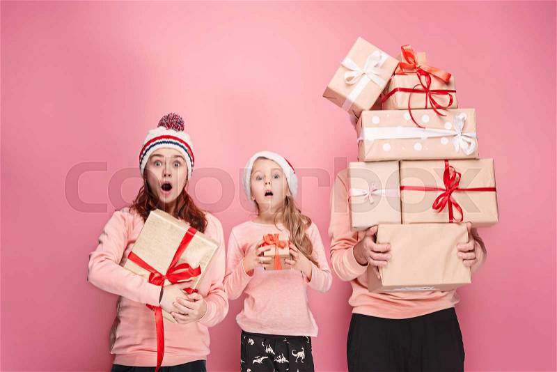 Father and mother give gifts to little daughter at pink studio background, stock photo